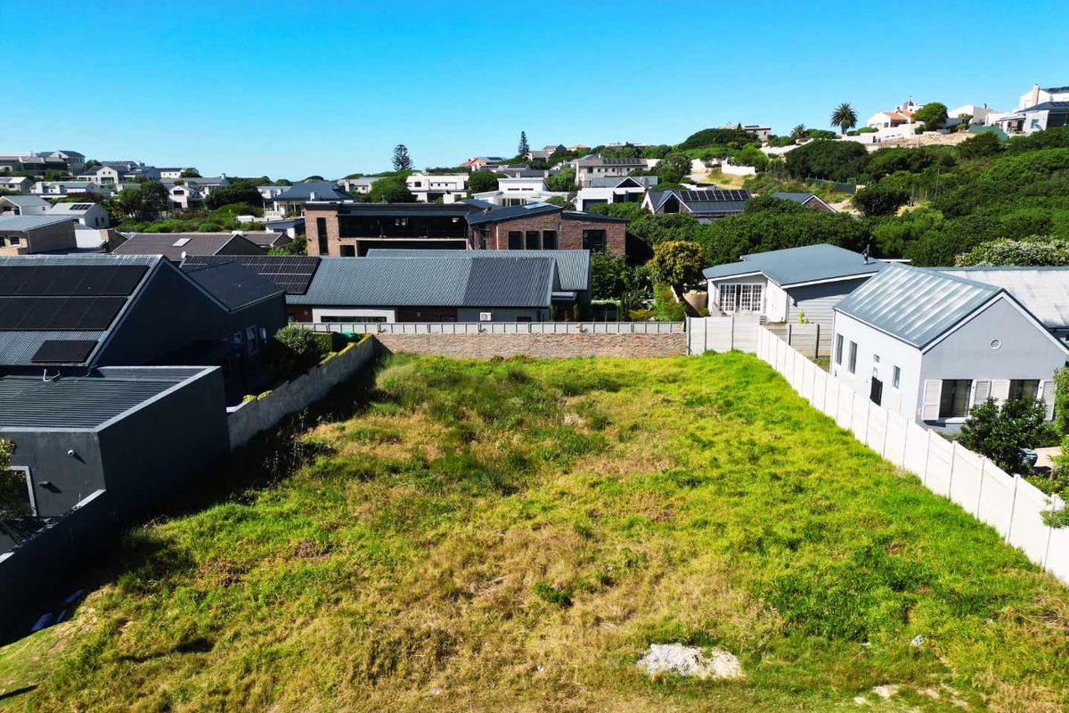 An aerial view of a vacant residential plot situated within an established suburban neighborhood, featuring boundary walls and surrounding residential properties.