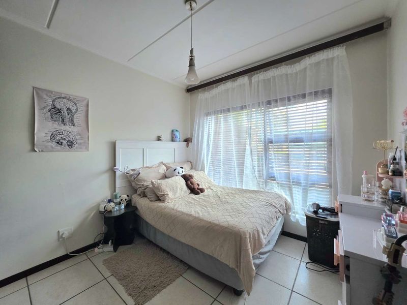 A functional bedroom featuring tiled flooring, a large window with curtain rod, and neutral wall finishes.
