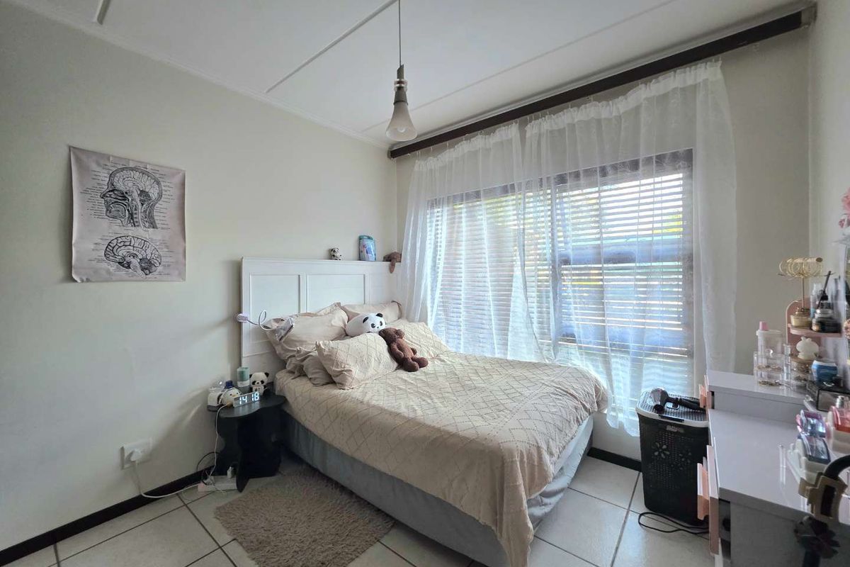 A functional bedroom featuring tiled flooring, a large window with curtain rod, and neutral wall finishes.