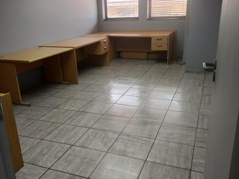 A functional office space featuring tiled flooring, a built-in desk configuration, drop ceiling with recessed lighting, and venetian blinds.