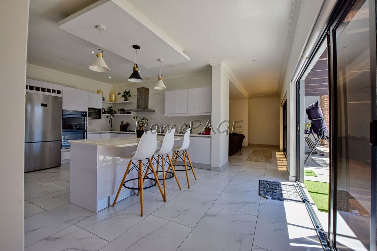 Modern open-plan kitchen featuring white cabinetry, a central island, built-in appliances, and large sliding glass doors leading to an outdoor patio area.