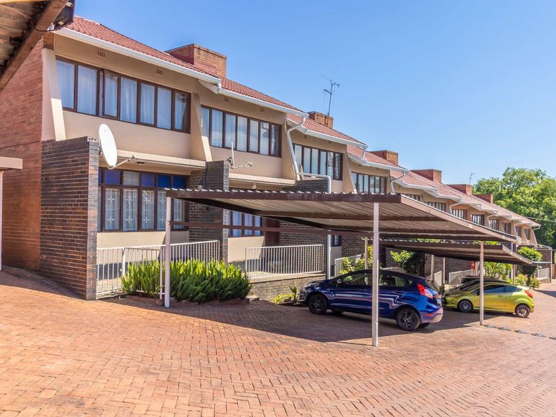Front elevation of a multi-story apartment complex featuring brick facade, tiled roofing, and covered carport parking spaces on a paved driveway.