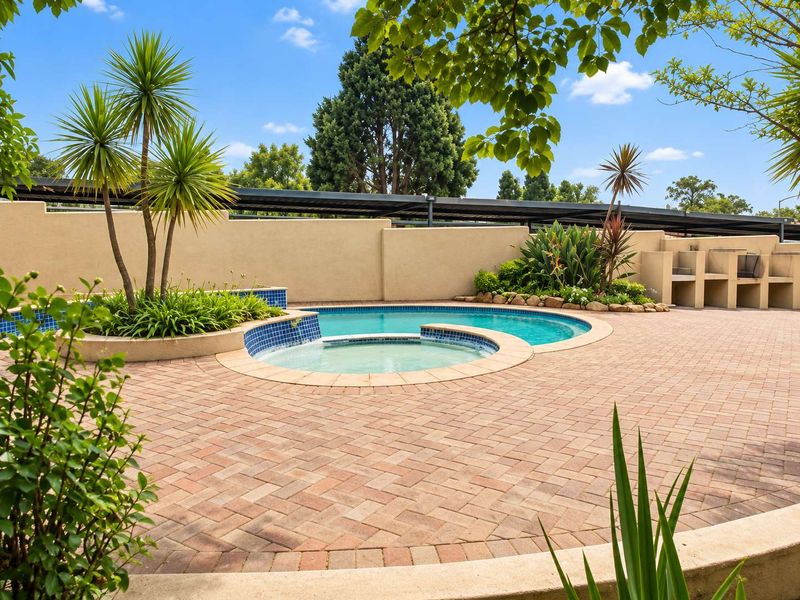 A well-maintained outdoor pool area featuring a swimming pool, integrated spa, paved patio, and a built-in braai station.