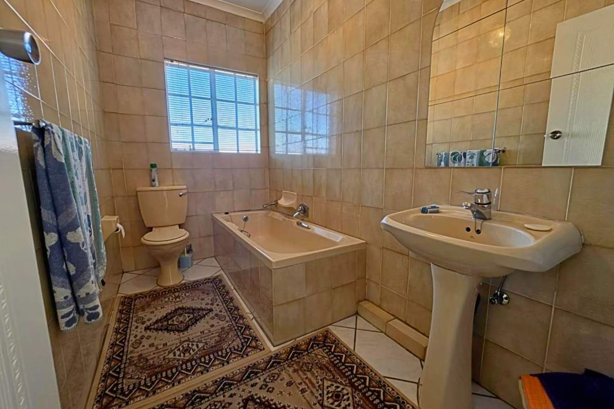 A functional bathroom featuring a built-in bathtub, pedestal basin, and toilet, finished with floor-to-ceiling ceramic wall tiles and tiled flooring.