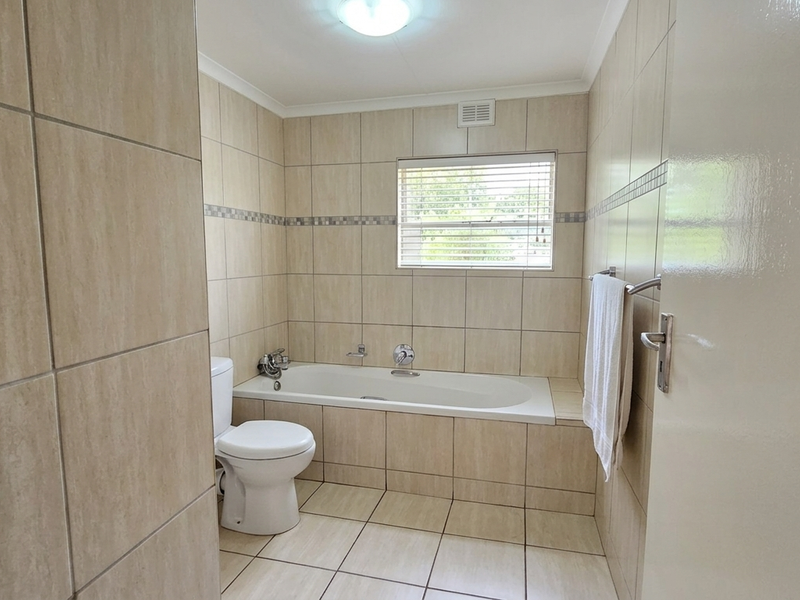 A functional bathroom featuring neutral ceramic tiling, a built-in bathtub, and a toilet, offering a clean and practical space.