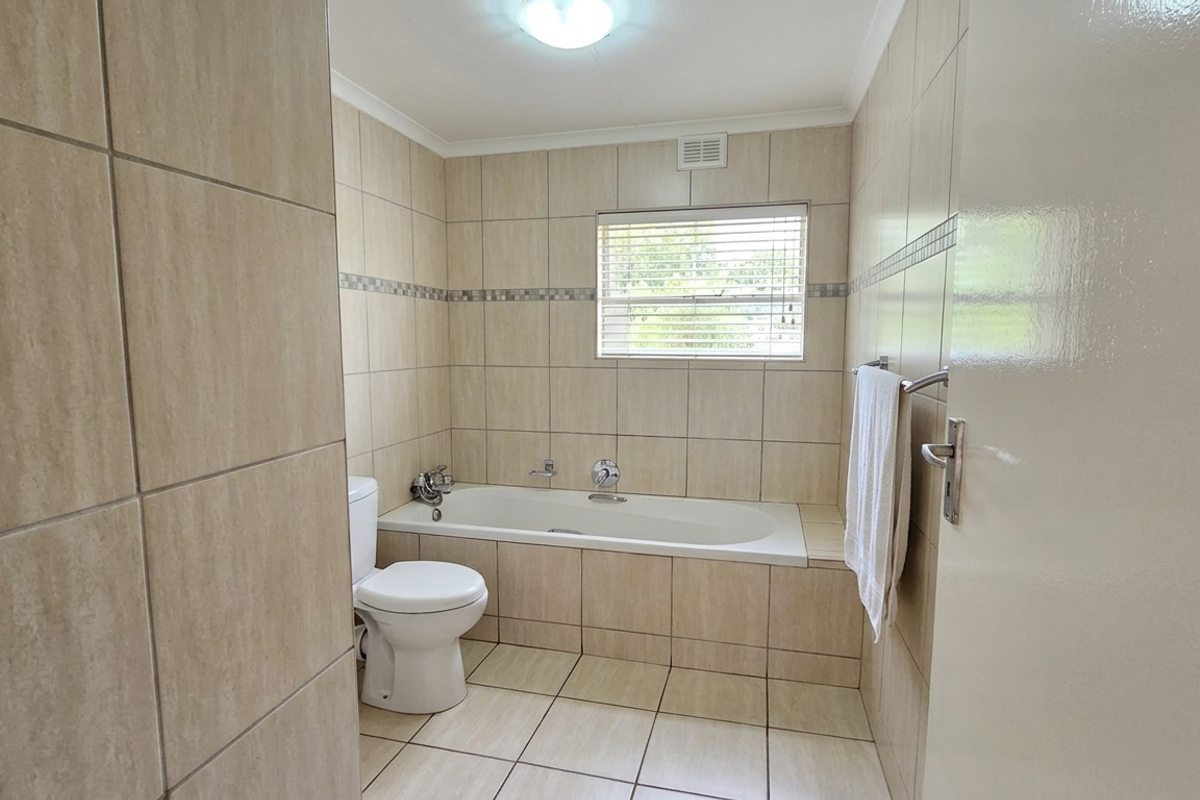 A functional bathroom featuring neutral ceramic tiling, a built-in bathtub, and a toilet, offering a clean and practical space.