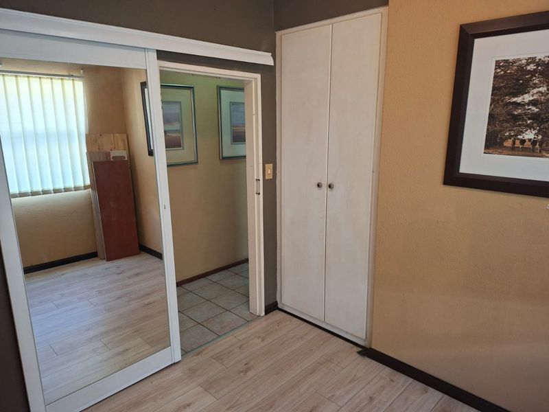 Bedroom featuring light laminate flooring, mirrored sliding wardrobe doors, and a built-in cupboard, offering a functional and neutral space.