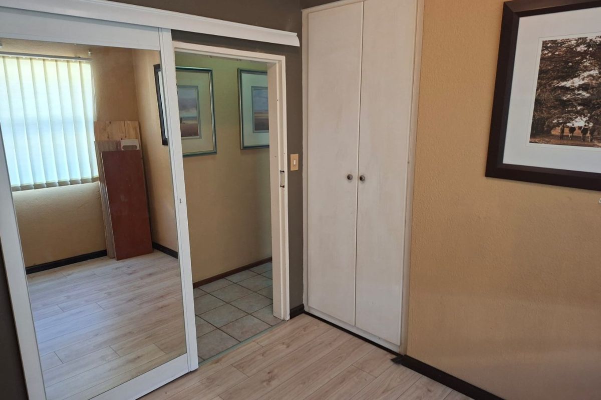 Bedroom featuring light laminate flooring, mirrored sliding wardrobe doors, and a built-in cupboard, offering a functional and neutral space.