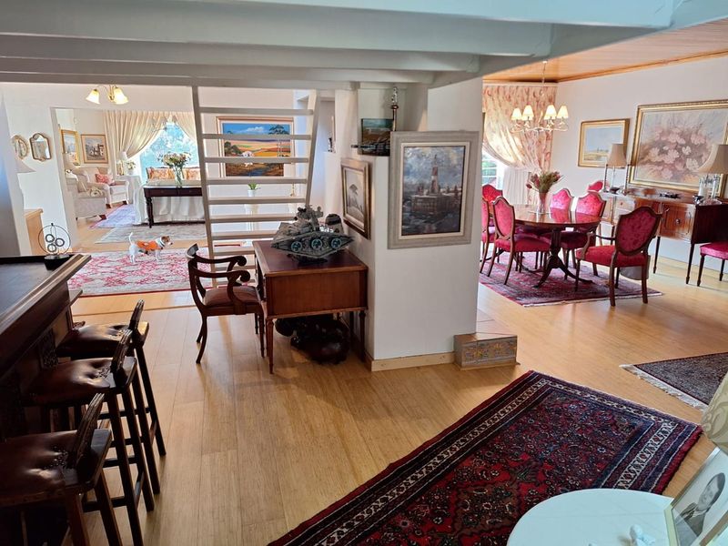 Spacious open-plan living and dining area featuring timber flooring, exposed ceiling beams, and a central staircase, creating a versatile and connected home layout.