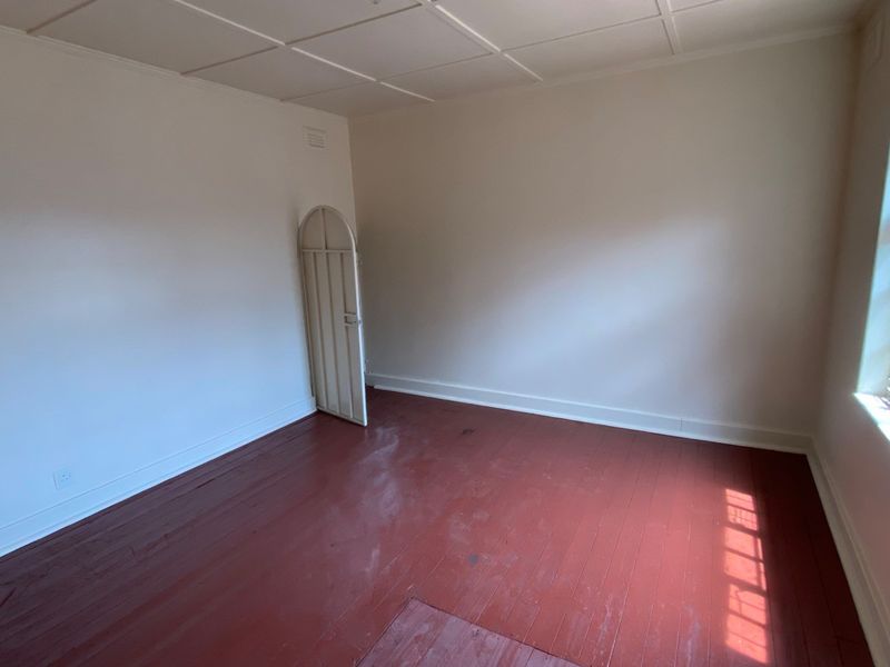 An empty bedroom featuring original timber flooring, a security gate, and a leaded glass window, offering a blank canvas for renovation.