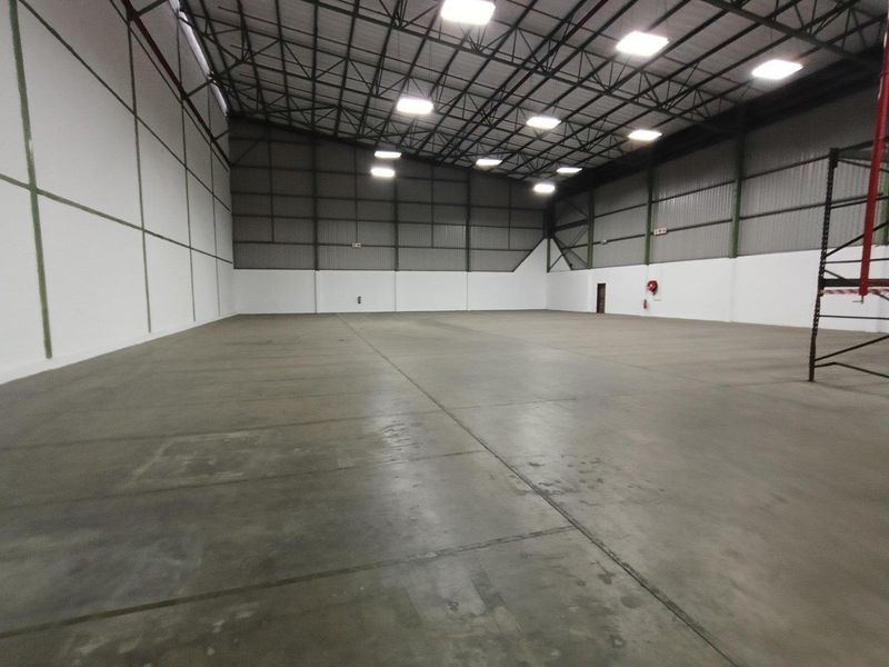 Spacious industrial warehouse unit featuring high ceilings, exposed steel trusses, polished concrete flooring, and high-bay lighting, suitable for storage or manufacturing operations.