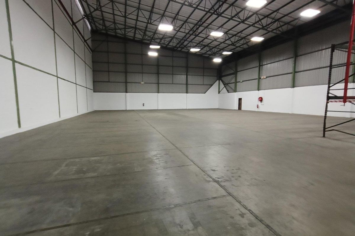Spacious industrial warehouse unit featuring high ceilings, exposed steel trusses, polished concrete flooring, and high-bay lighting, suitable for storage or manufacturing operations.