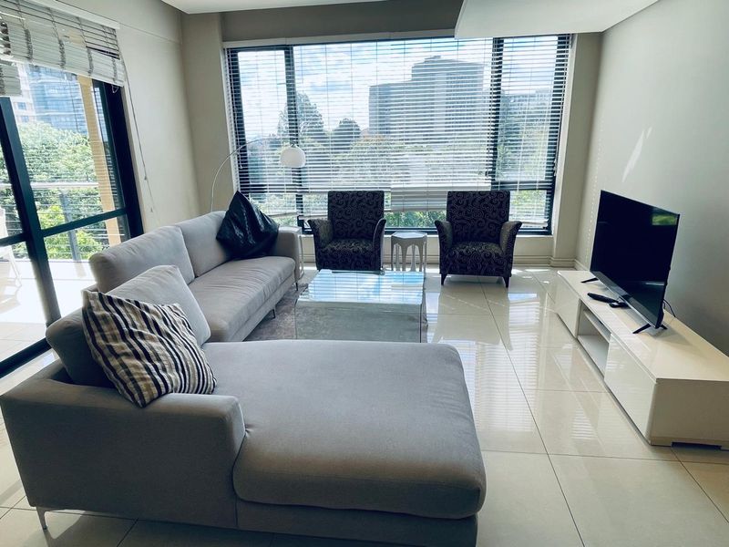 A bright and modern living room featuring large format floor tiles, expansive floor-to-ceiling windows, and direct access to a balcony.