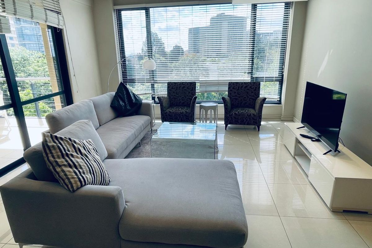 A bright and modern living room featuring large format floor tiles, expansive floor-to-ceiling windows, and direct access to a balcony.