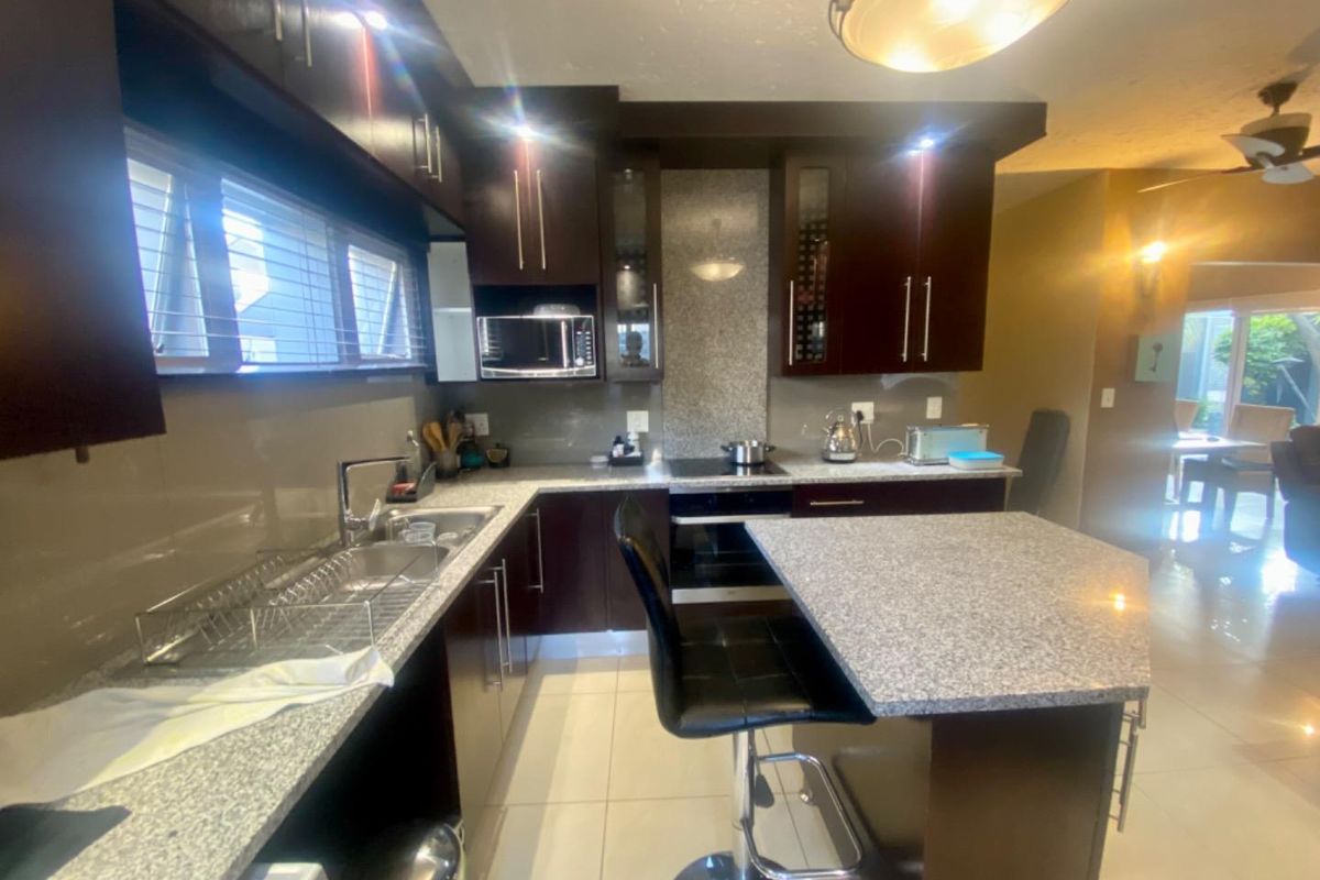 Modern kitchen featuring dark wood cabinetry, granite countertops, a central island with breakfast bar seating, and integrated stainless steel appliances.