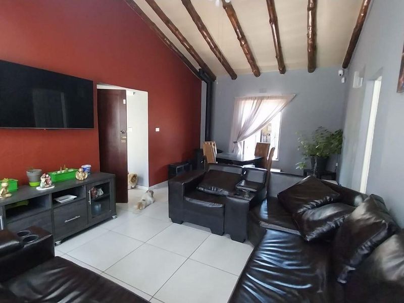 Spacious living room featuring a vaulted ceiling with exposed timber beams and neutral tiled flooring.