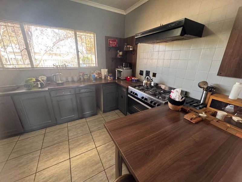 A functional kitchen featuring dark cabinetry, wood-look laminate countertops, a gas stove with extractor fan, and tiled flooring.