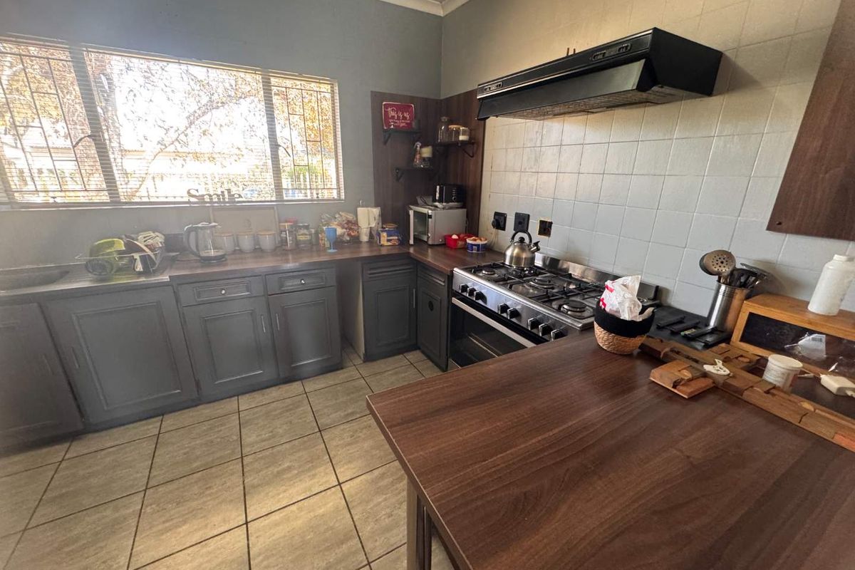 A functional kitchen featuring dark cabinetry, wood-look laminate countertops, a gas stove with extractor fan, and tiled flooring.