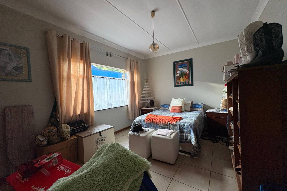A functional bedroom featuring tiled flooring, neutral wall finishes, and a central pendant light fixture with natural light from the window.