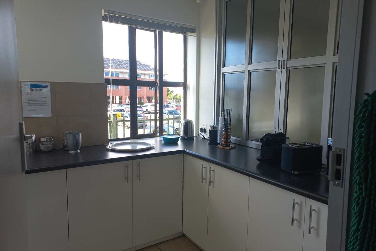 A compact office kitchenette featuring white cabinetry, dark countertops, and a window providing natural light and views of the parking area.