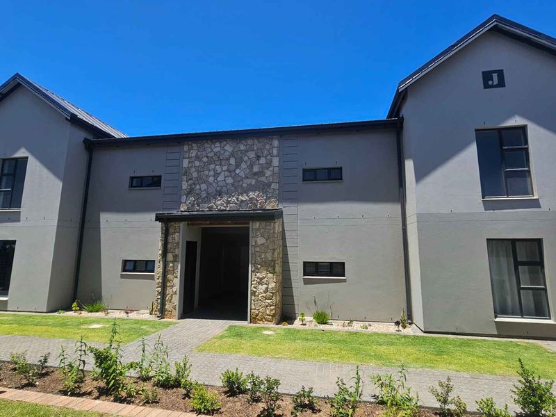 Front elevation of a modern apartment building featuring stone cladding accents, paved walkways, and well-maintained lawn areas under a clear blue sky.