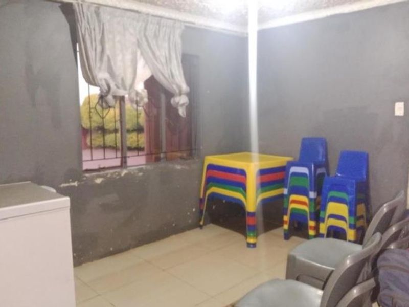 A living area featuring tiled flooring and security bars on the window, currently showing signs of wear on the wall surfaces.