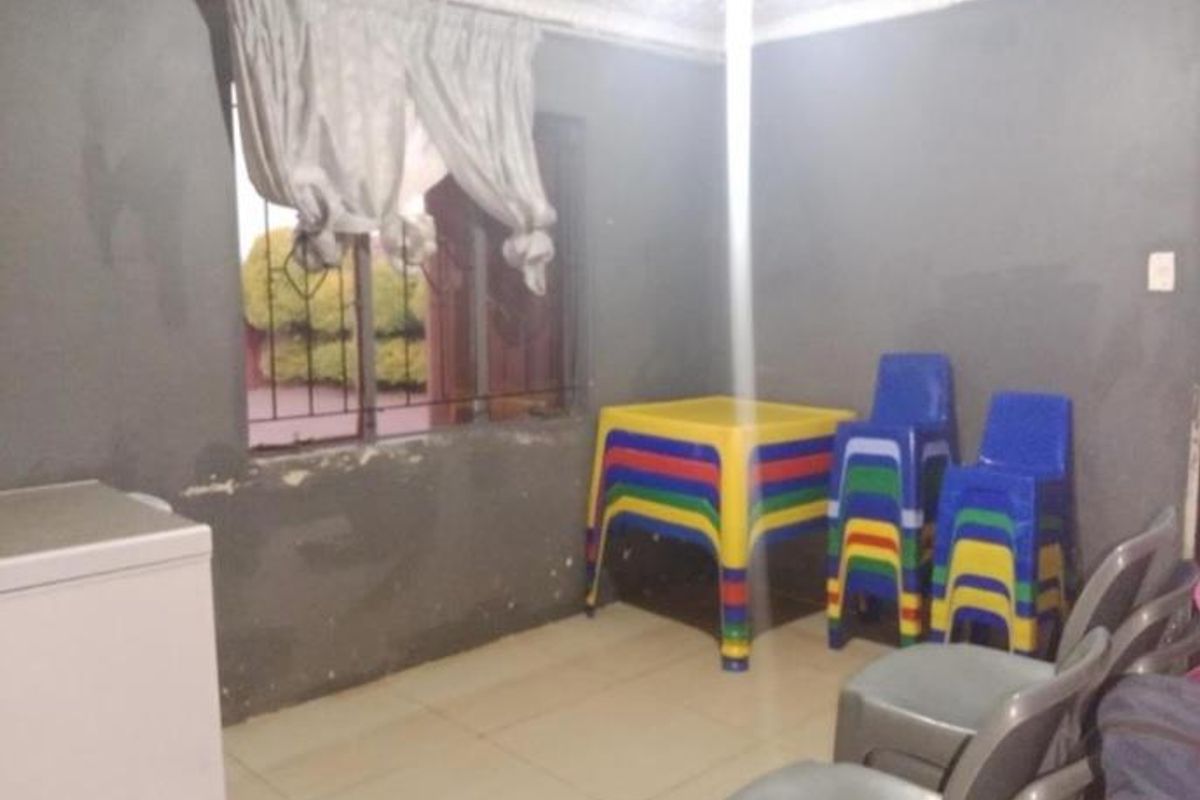 A living area featuring tiled flooring and security bars on the window, currently showing signs of wear on the wall surfaces.