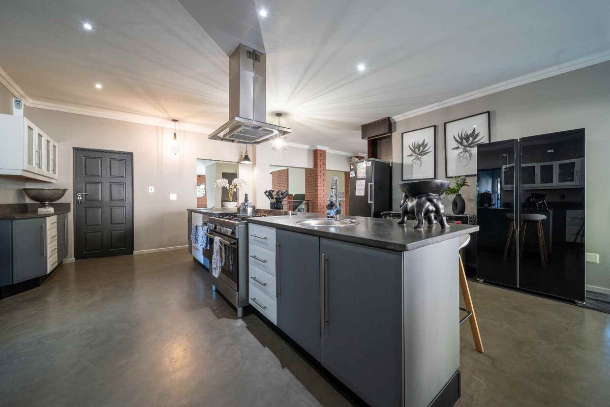 Modern kitchen featuring a central island with a sink, stainless steel gas stove, extractor fan, and sleek cabinetry with dark countertops.