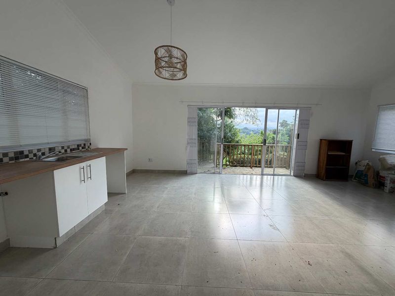 Open-plan living area featuring a kitchenette with wooden countertops, tiled flooring, and sliding doors leading to an outdoor deck with scenic views.