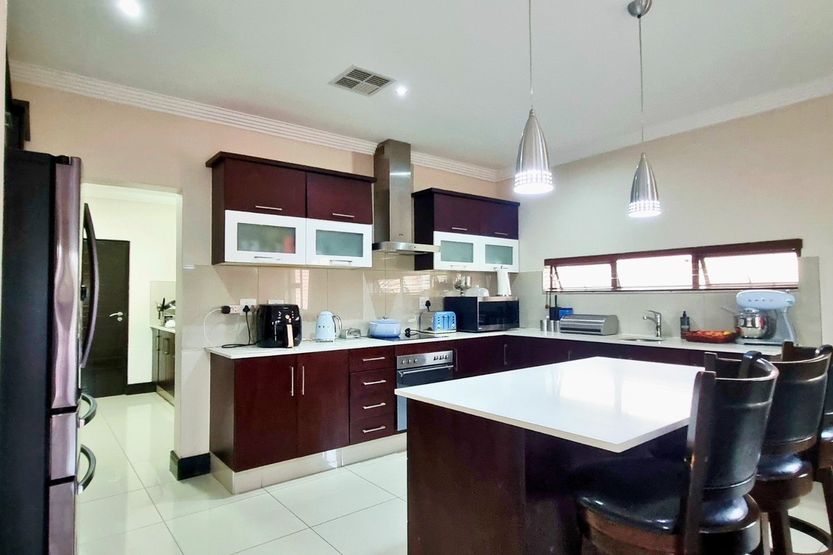 A well-maintained kitchen featuring dark wood cabinetry, a central island with seating, stainless steel appliances, and tiled flooring.