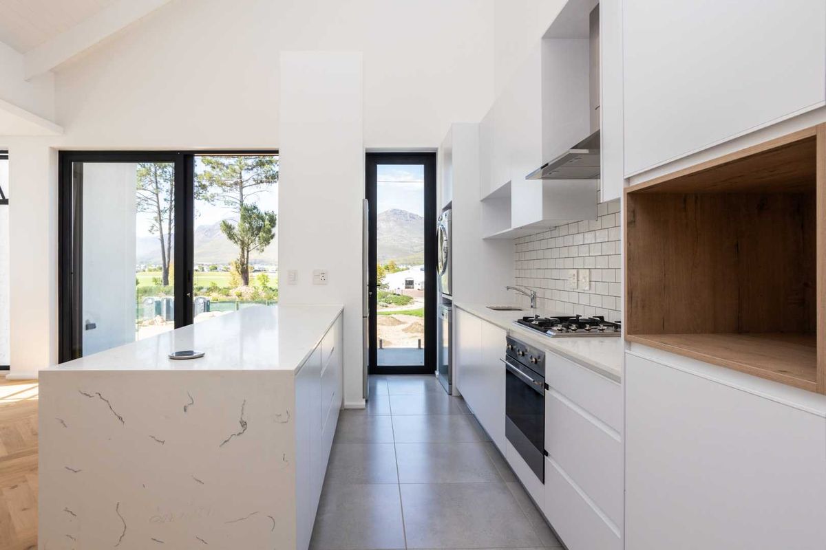 Modern kitchen featuring white cabinetry, stone countertops, a central island, built-in oven, gas hob, and subway tile backsplash with views of the surrounding landscape.