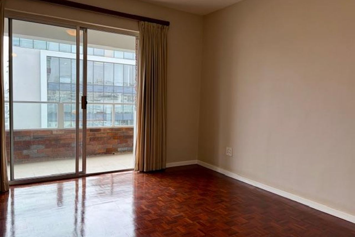 An empty bedroom featuring polished parquet flooring and a large sliding glass door providing access to an outdoor balcony area.