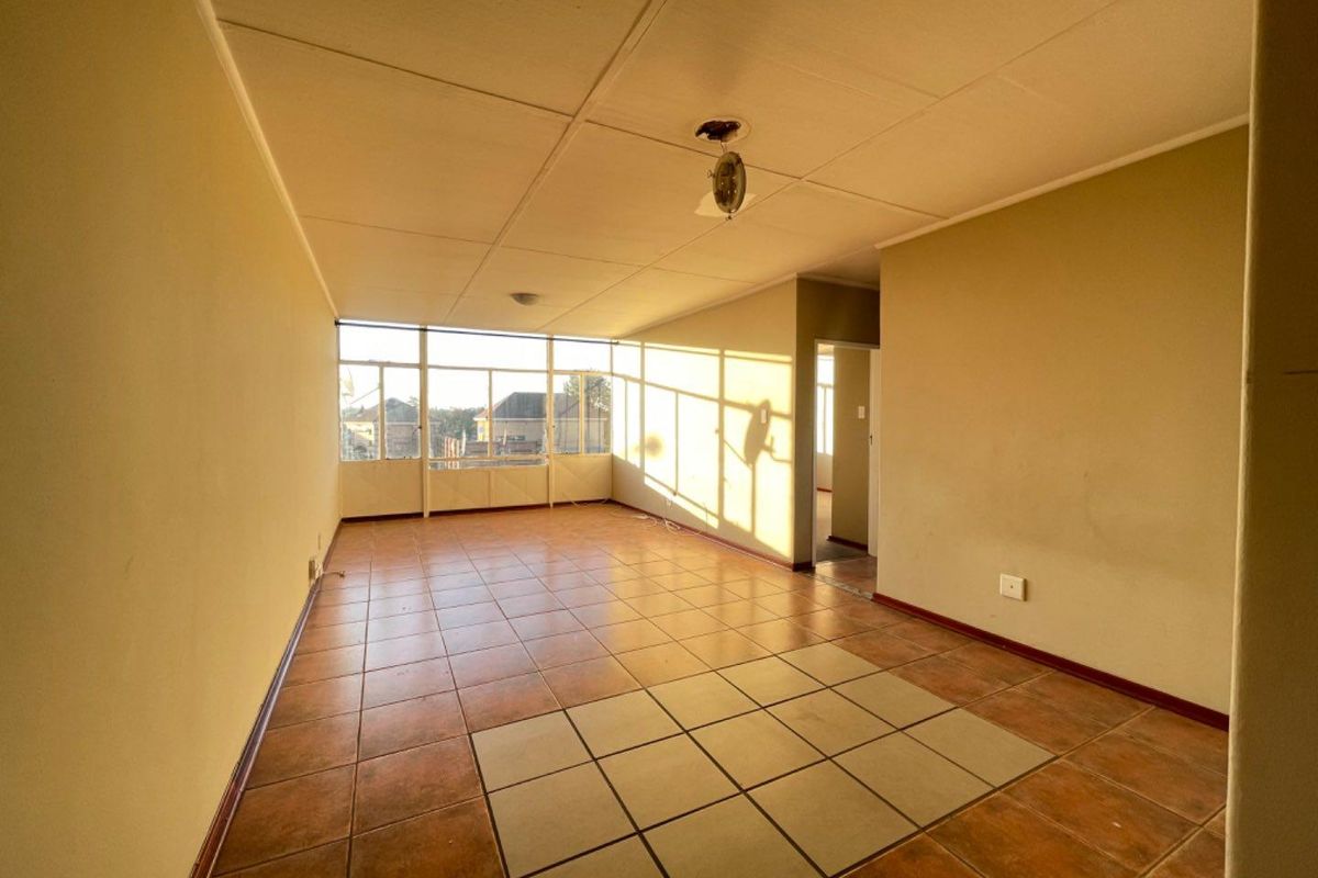 An empty, sunlit living area featuring tiled flooring and large windows, offering a blank canvas for renovation and interior design.