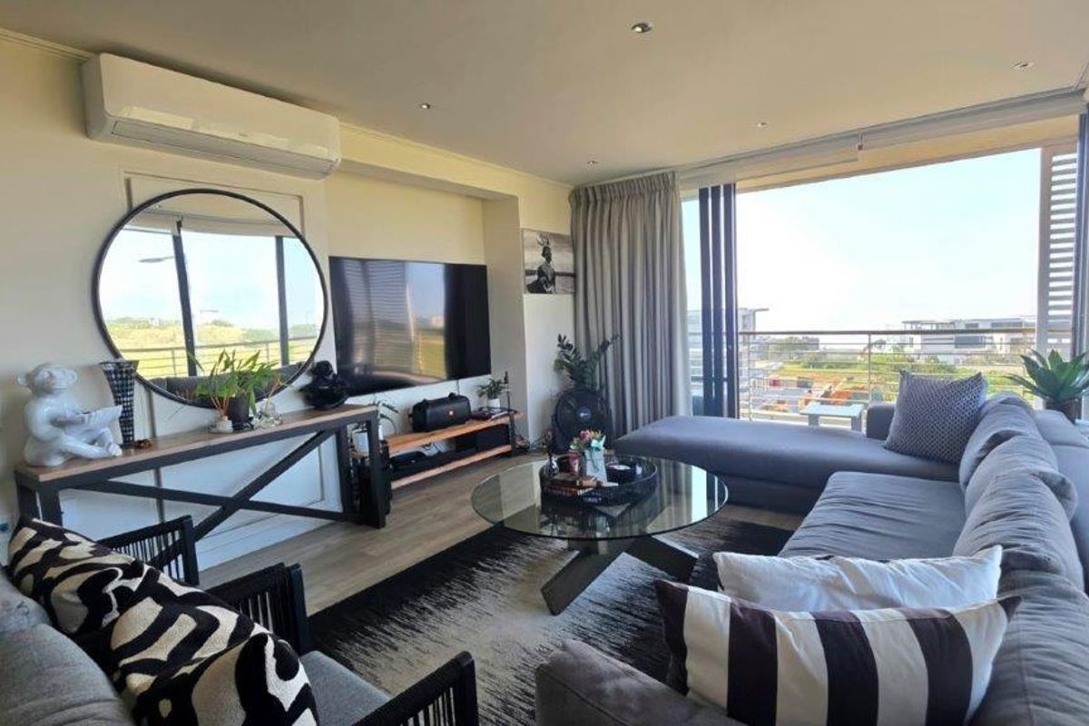 A bright and modern living room featuring laminate flooring, recessed lighting, a wall-mounted air conditioner, and large sliding doors leading to a balcony.
