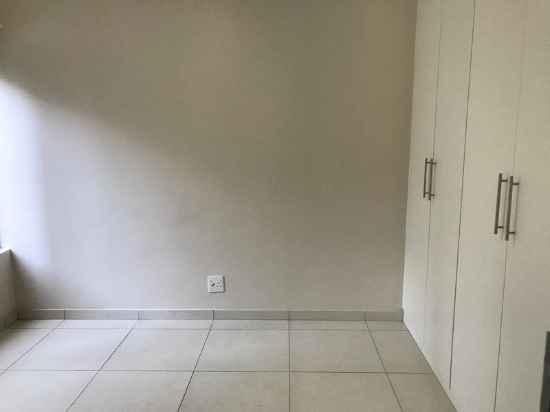 A clean, empty bedroom featuring neutral tiled flooring and white built-in cupboards, providing a blank canvas for personalization.