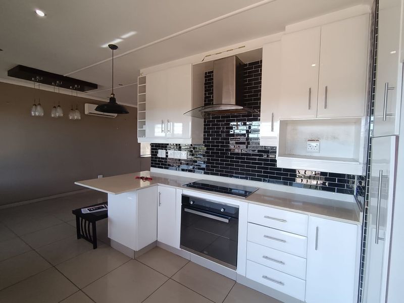 Modern open-plan kitchen featuring white cabinetry, stone countertops, subway tile backsplash, and integrated appliances, seamlessly flowing into the adjacent living area.