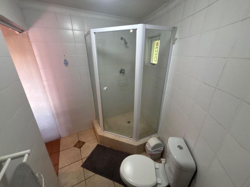 A functional bathroom featuring a corner shower enclosure, ceramic tiling throughout, and a standard toilet, presenting a clean but dated aesthetic.