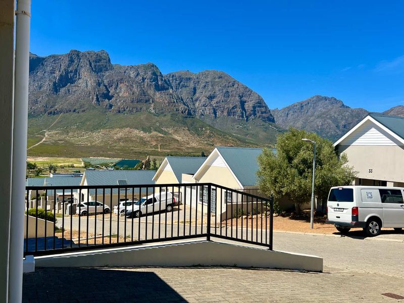 A scenic view overlooking a residential estate with paved driveways, pitched roof homes, and a prominent mountain backdrop.