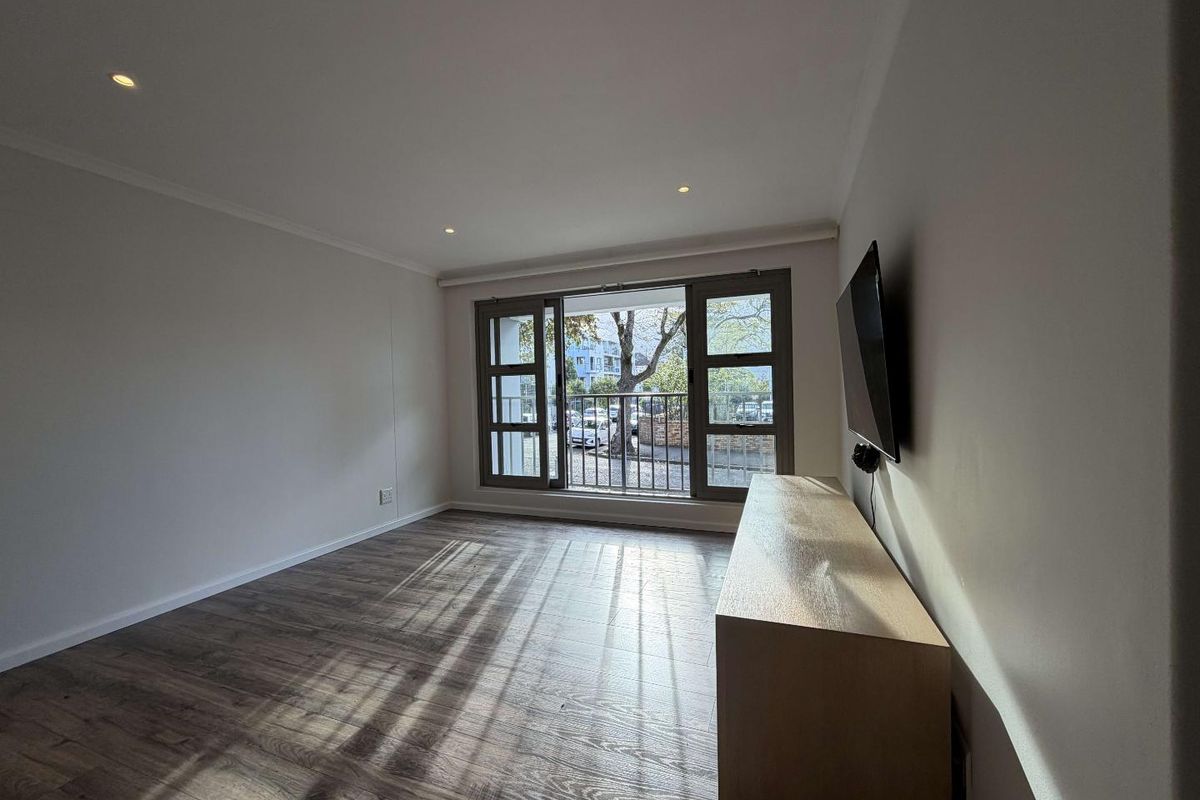 A bright and spacious living room featuring modern wood-look flooring, recessed ceiling lighting, and large windows with a view.