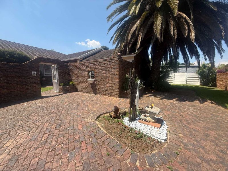 Front entrance area featuring a brick-paved driveway, established palm tree, and secure brick boundary wall with a gated entry.