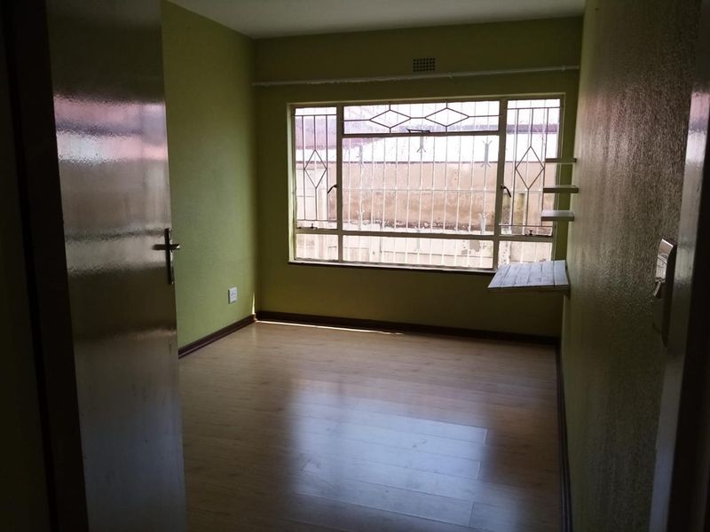 An empty bedroom featuring laminate flooring, a built-in wall shelf, and security bars on the window.