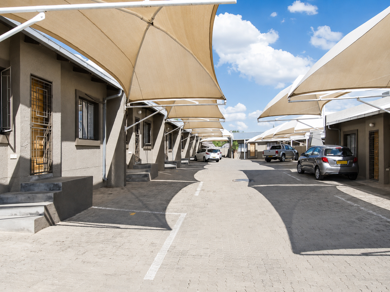 A well-maintained townhouse complex parking area featuring paved driveways and overhead shade sail structures for vehicle protection.
