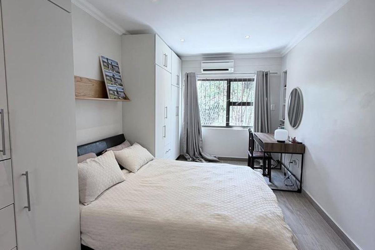 A well-maintained bedroom featuring built-in cabinetry, recessed ceiling lighting, and a wall-mounted air conditioning unit.