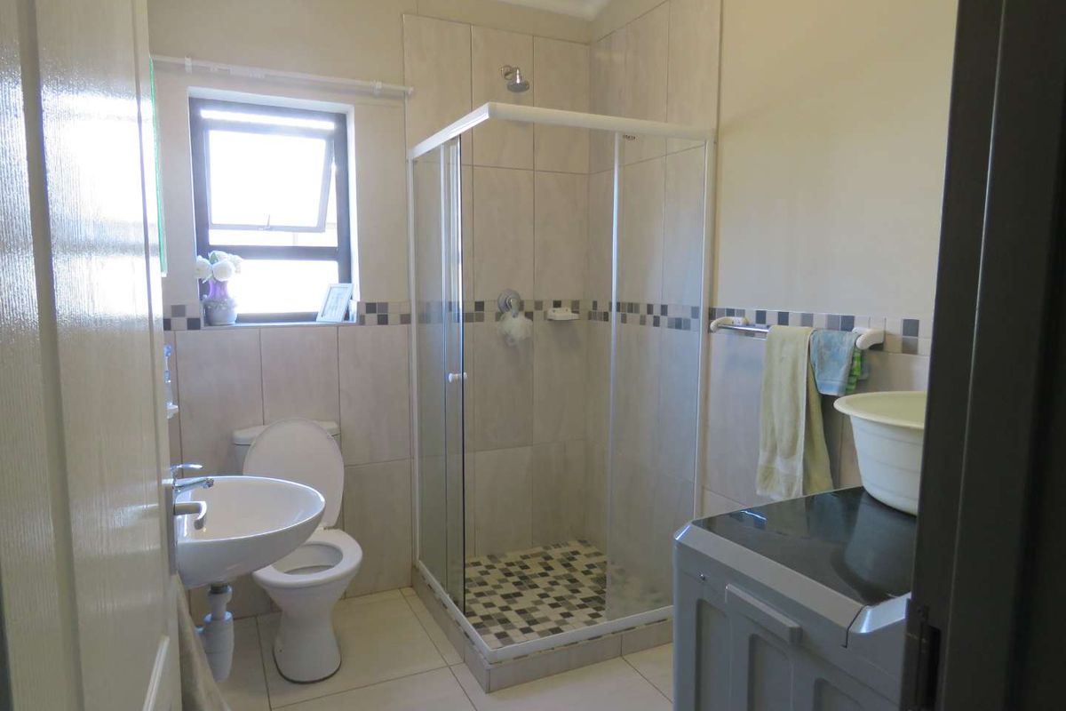 A functional bathroom featuring a glass-enclosed shower, pedestal basin, and toilet with neutral wall and floor tiling.