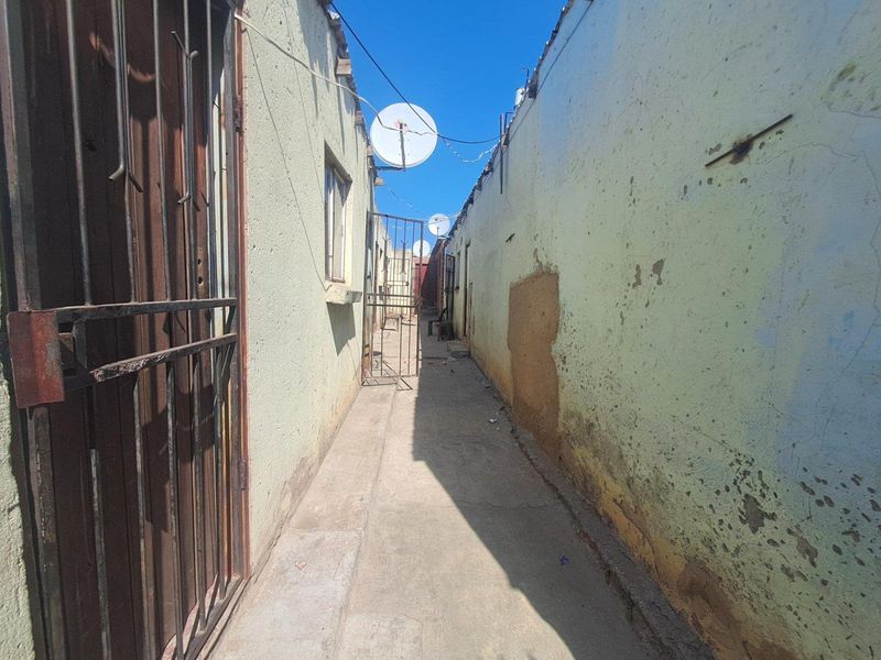 A narrow exterior side passage between two structures featuring concrete flooring, security gates, and visible wear to the exterior wall finishes.