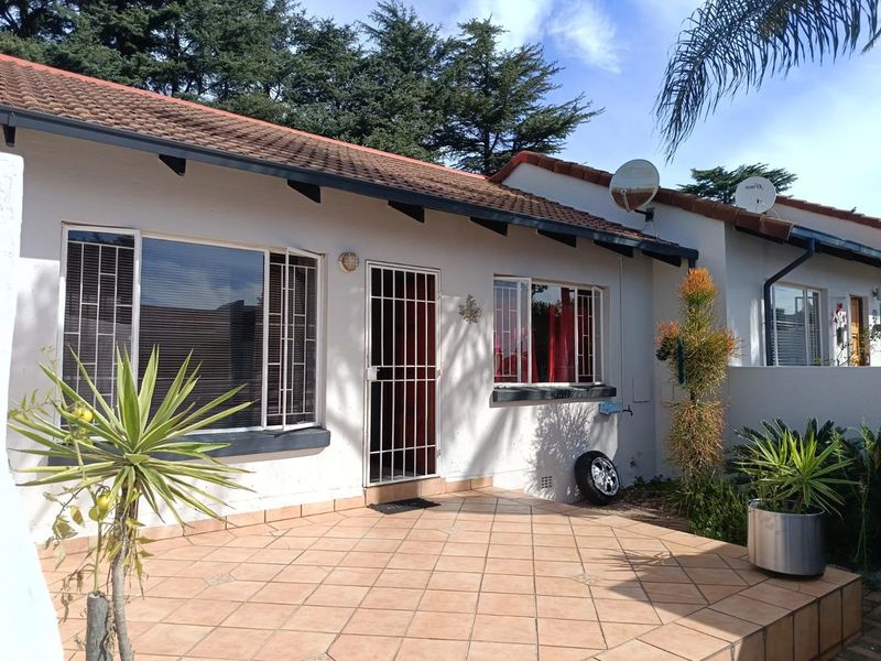 A view of the rear exterior of the townhouse featuring a tiled patio area, security gate, and tiled roof.