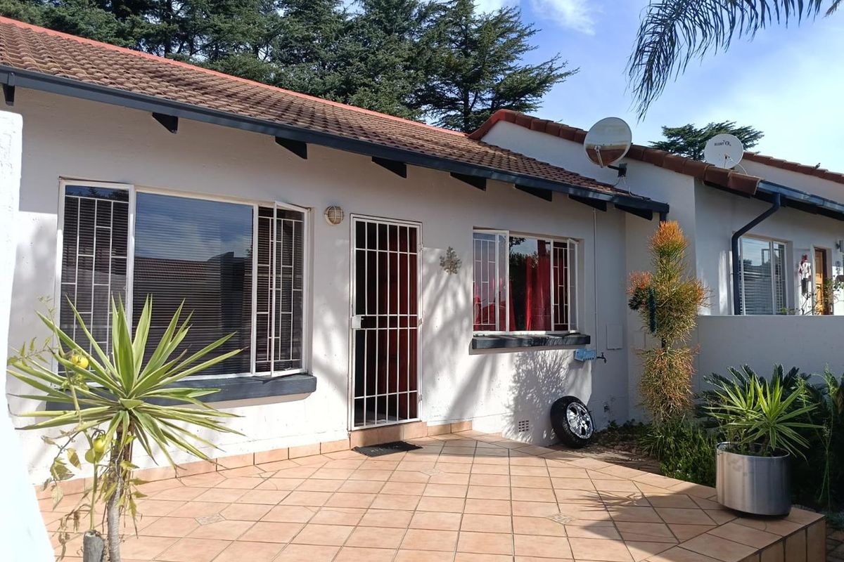 A view of the rear exterior of the townhouse featuring a tiled patio area, security gate, and tiled roof.