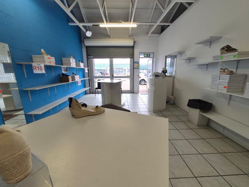 A functional office or retail space featuring tiled flooring, exposed ceiling trusses, and wall-mounted shelving, with a roller shutter door for secure access.
