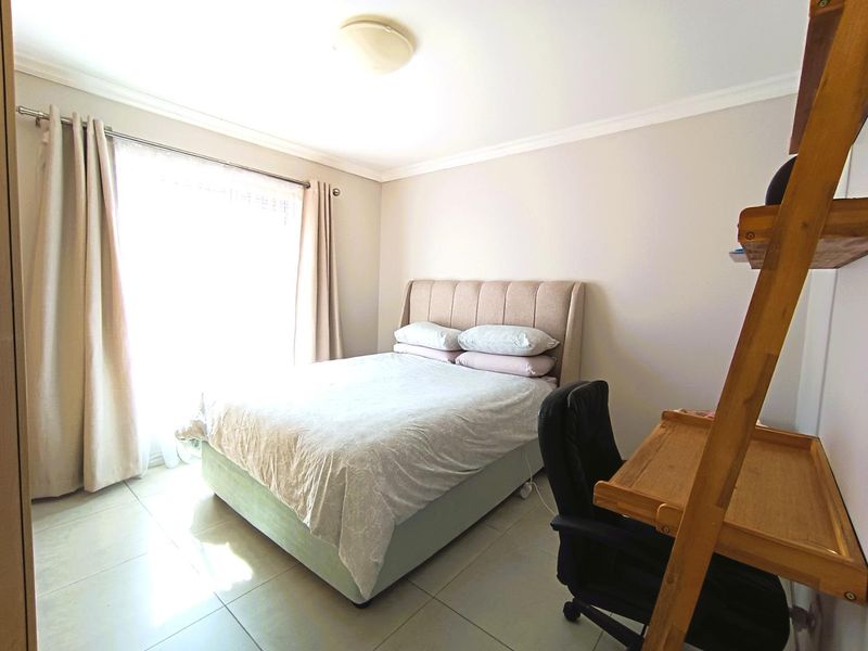 A well-lit bedroom featuring neutral wall tones, tiled flooring, and classic ceiling cornicing, providing a comfortable and functional living space.