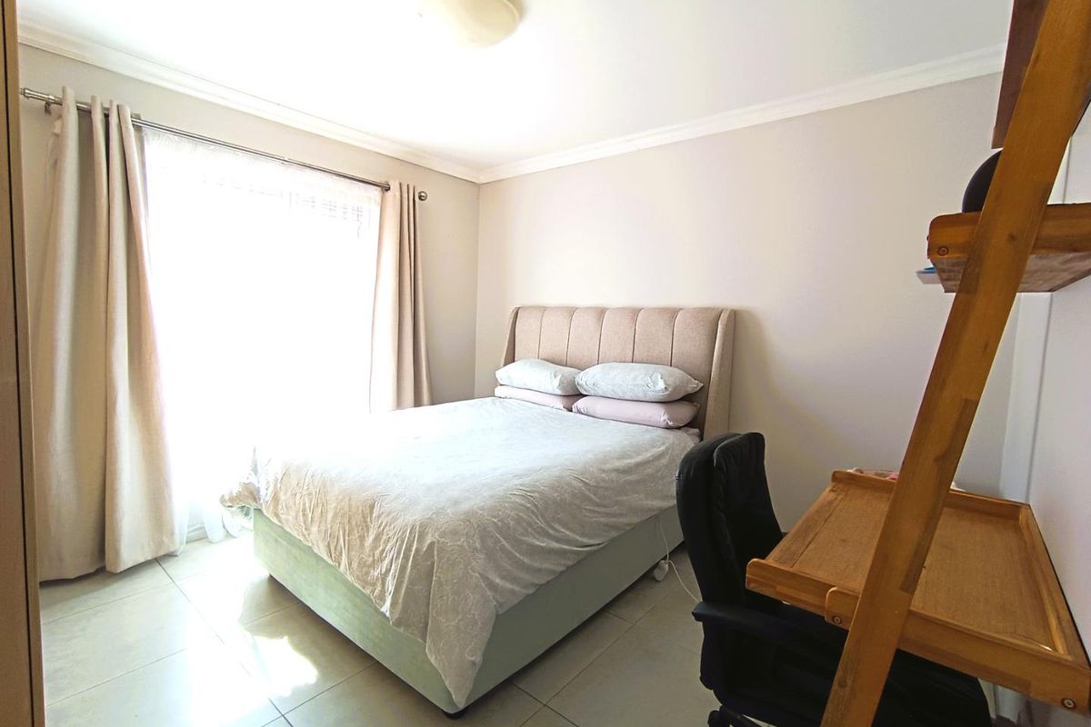 A well-lit bedroom featuring neutral wall tones, tiled flooring, and classic ceiling cornicing, providing a comfortable and functional living space.